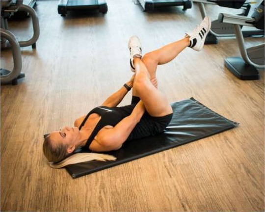 Lying figure-four glute stretch pulling the knee towards the chest